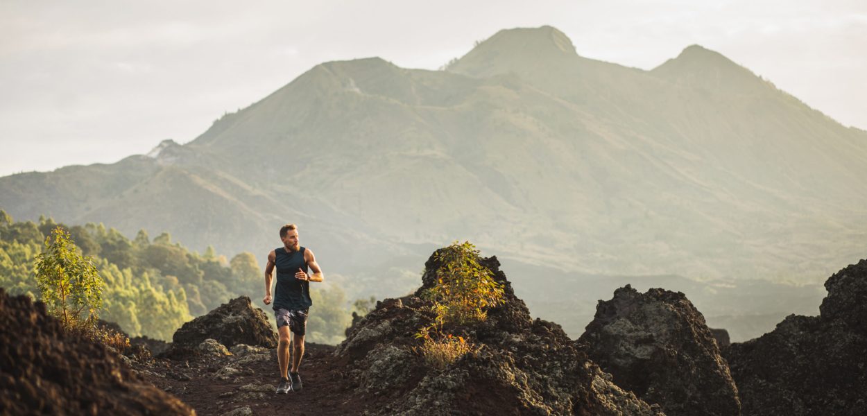 Young athlete man trail running in mountains in the morning. Amazing volcanic landscape of Bali mount Batur on background. Healthy lifestyle concept.